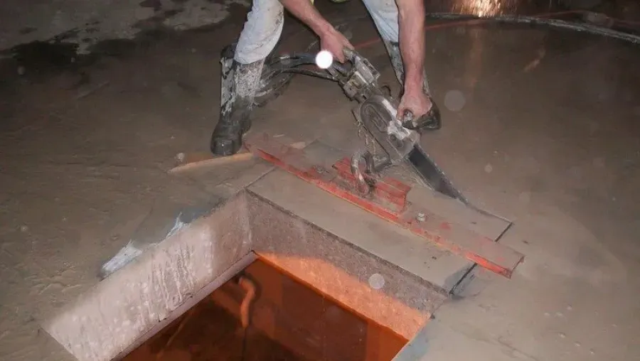 Person using a tool to level wet concrete near a square opening, indoor setting.