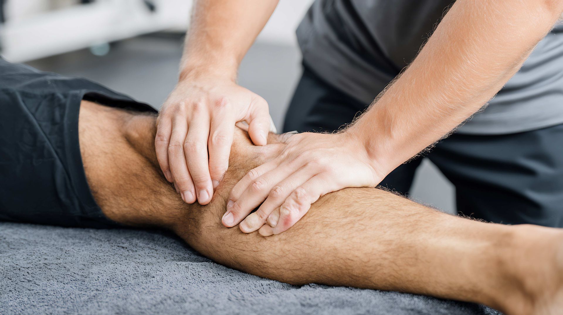 Hands massaging a person’s knee on a gray surface, suggesting physical therapy or injury treatment Hands massaging a person’s knee on a gray surface, suggesting physical therapy or injury treatment