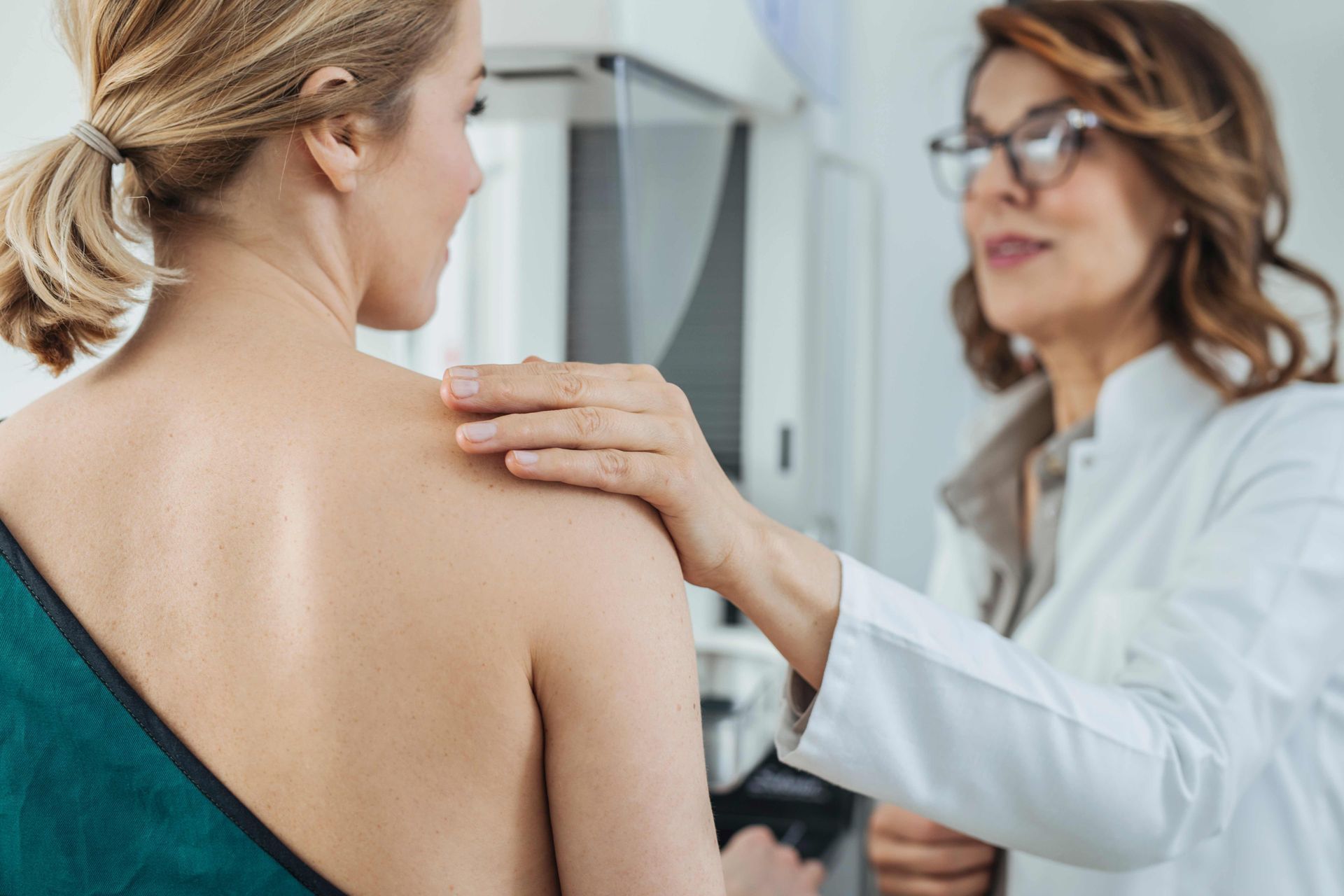 Doctor examining a patient’s back in a clinic, with a hand on her shoulder Doctor examining a patient’s back in a clinic, with a hand on her shoulder