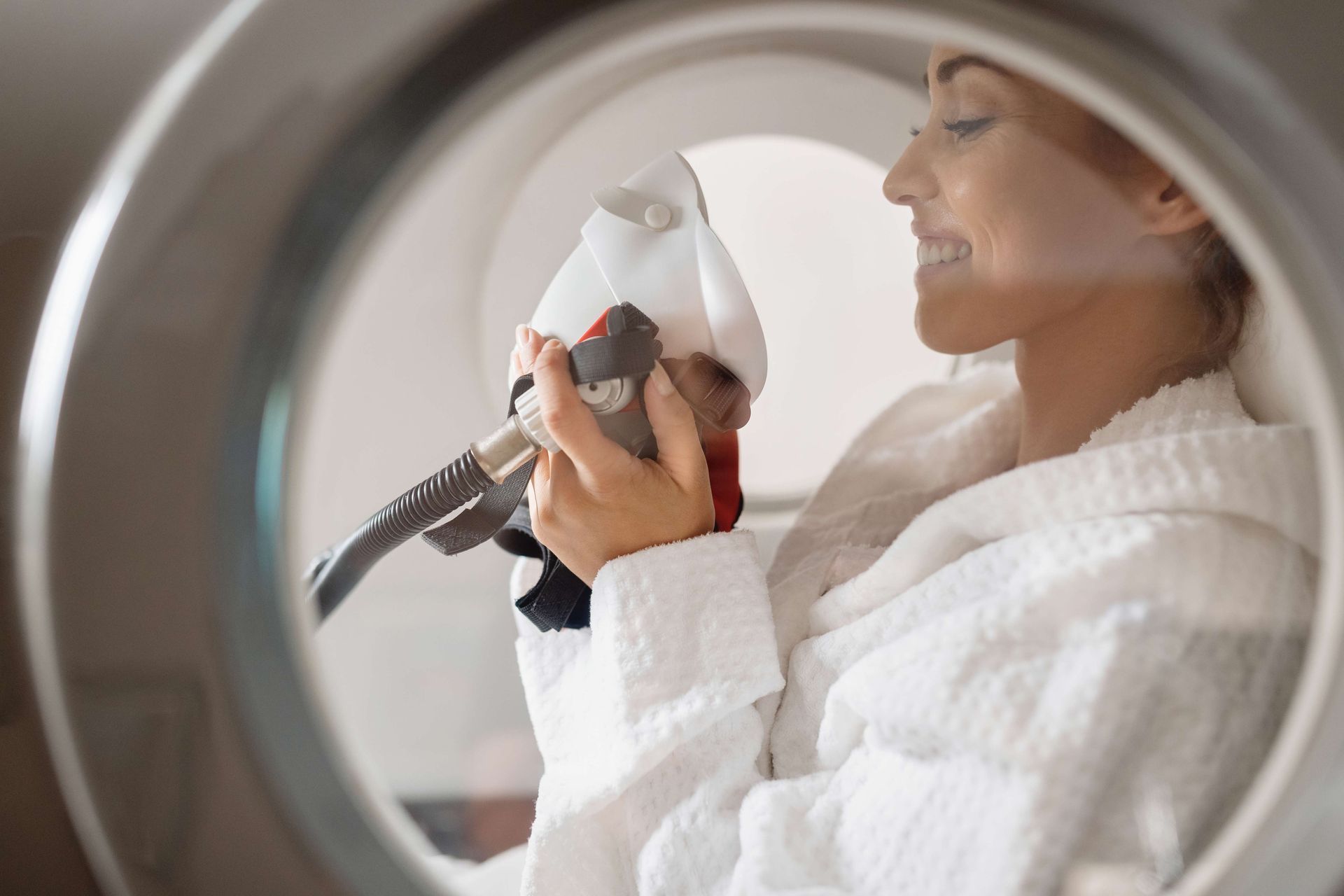 Person in a white robe using a handheld device inside a circular therapy or spa chamber