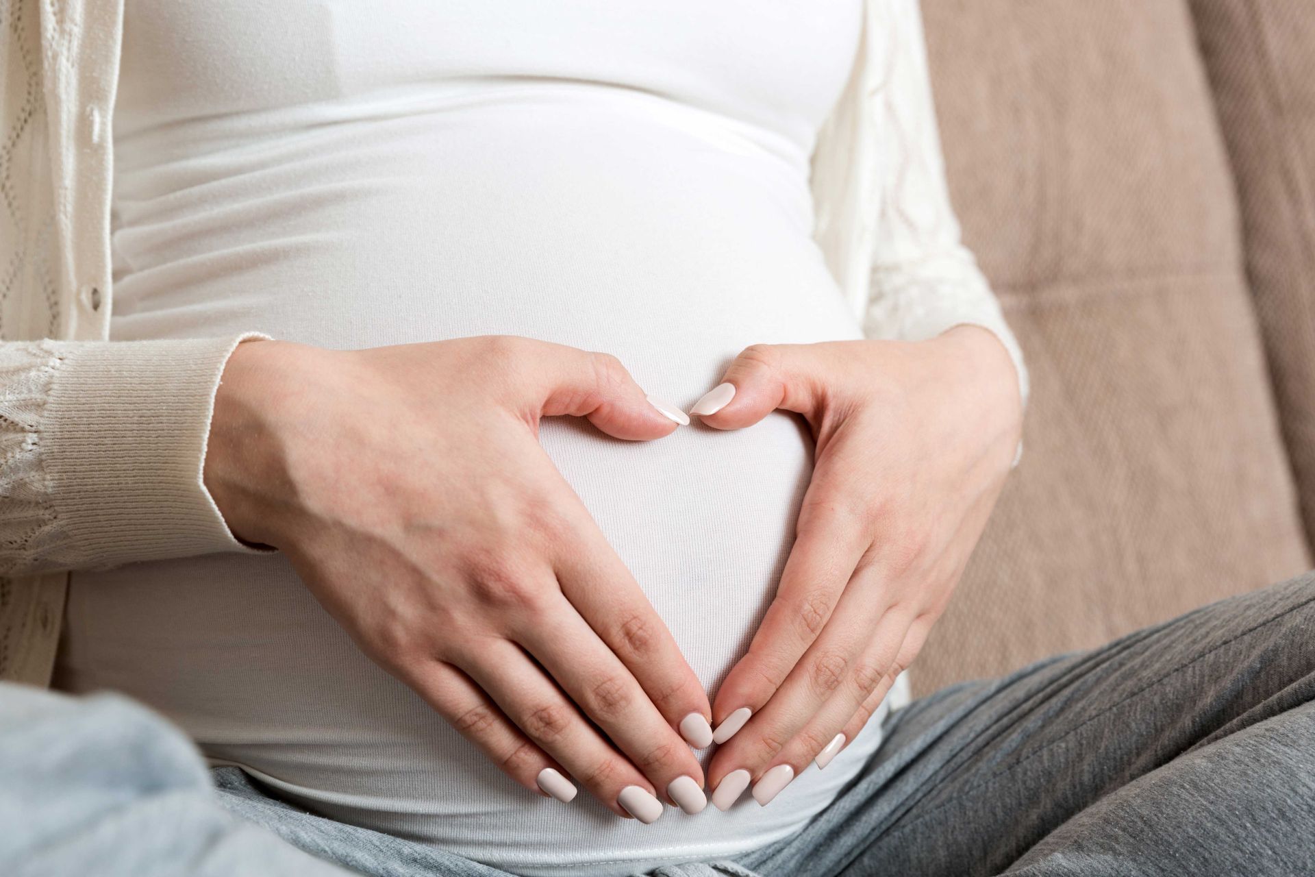 Hands forming a heart shape over a pregnant belly in a white shirt