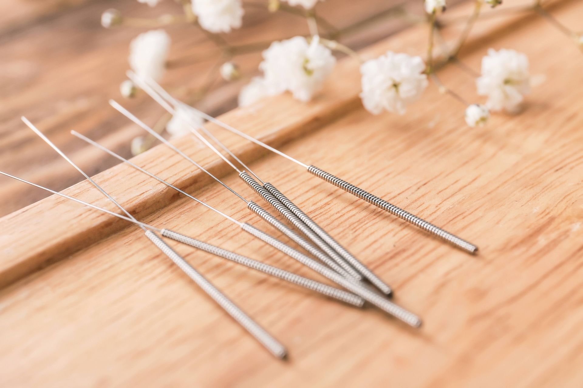 Metal acupuncture needles on a wooden surface with small white flowers in the background Metal acupuncture needles on a wooden surface with small white flowers in the background