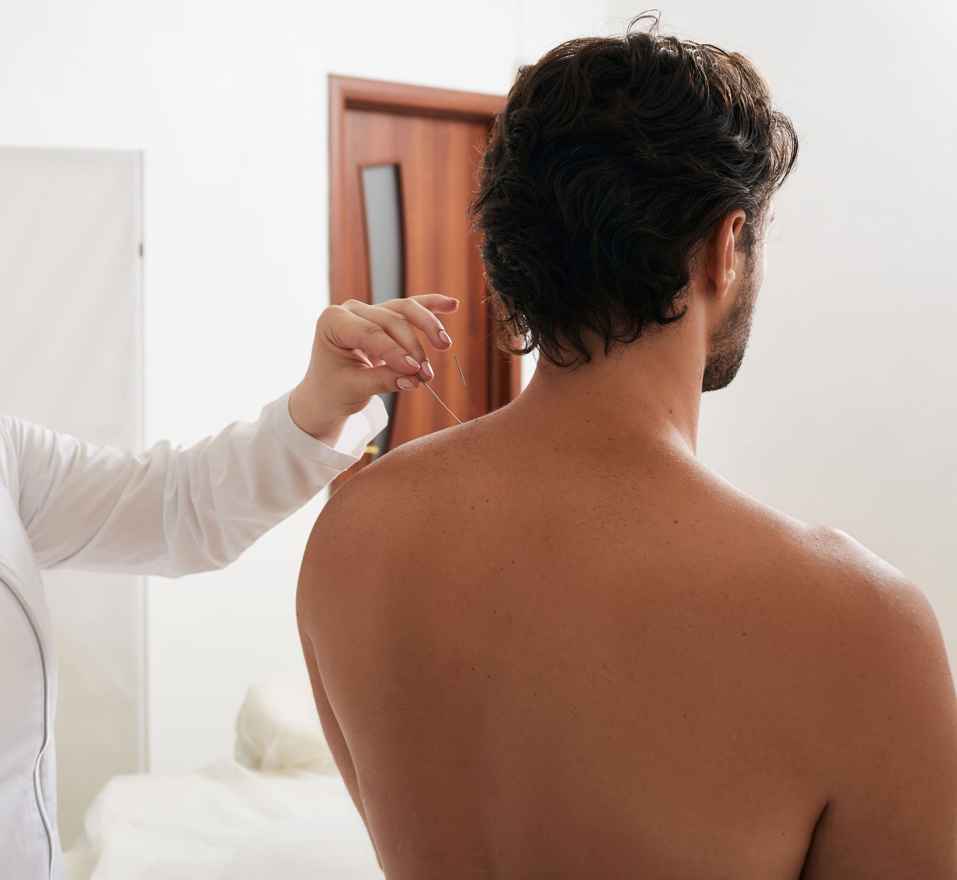 Doctor examining a patient’s back near a wooden door in a bedroom
