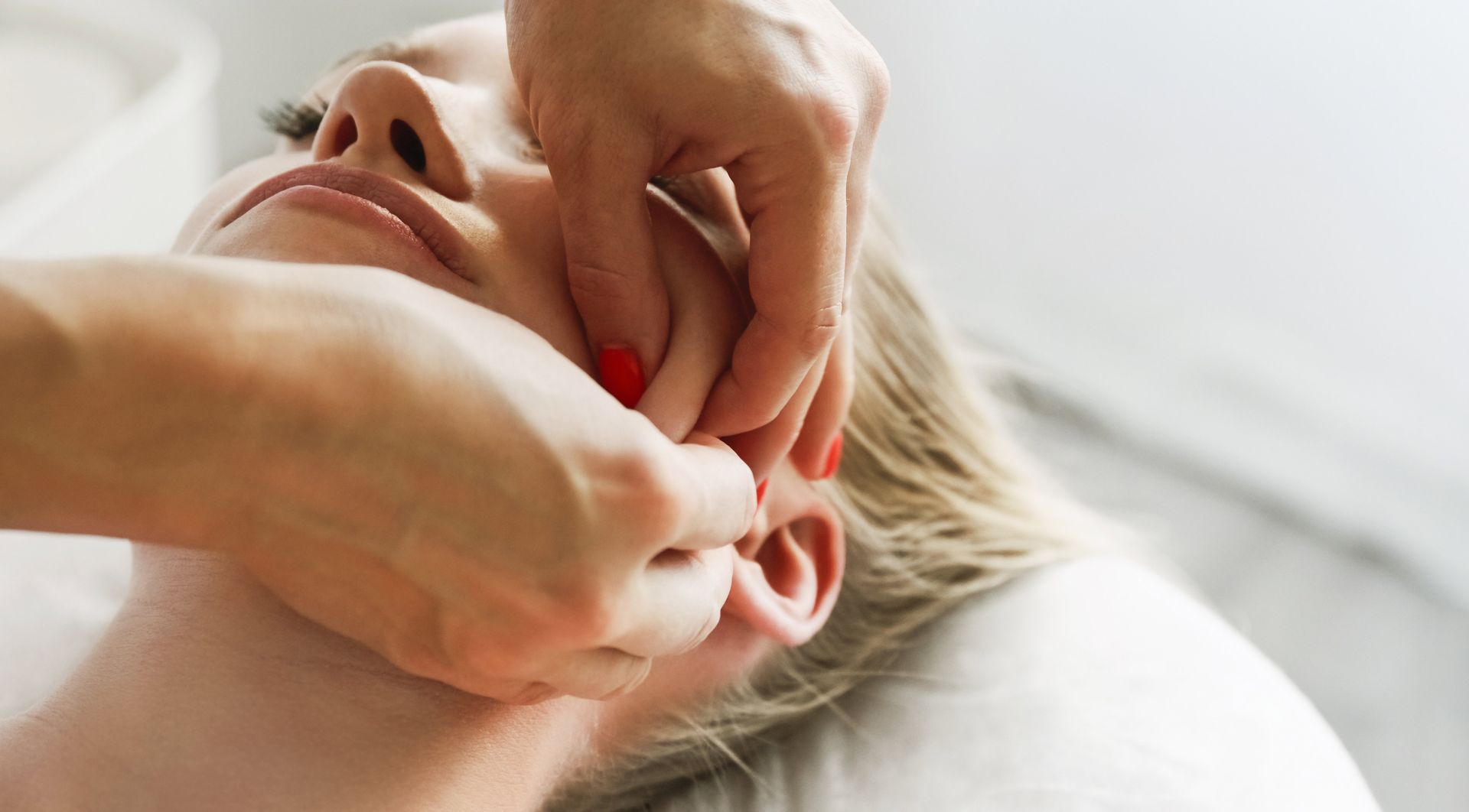 Hands pulling an ear to insert a red earring on a person lying on a pillow Hands pulling an ear to insert a red earring on a person lying on a pillow