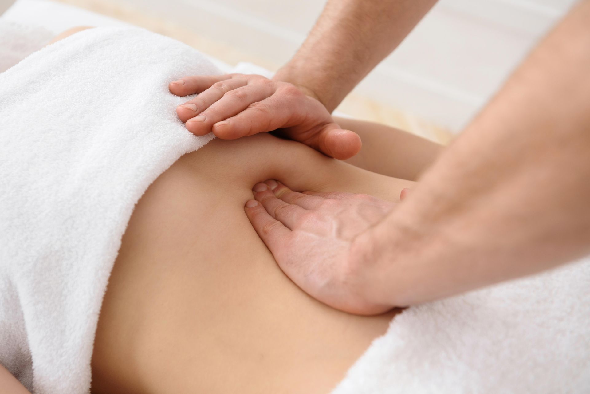 Hands giving a back massage on a person covered with a white towel