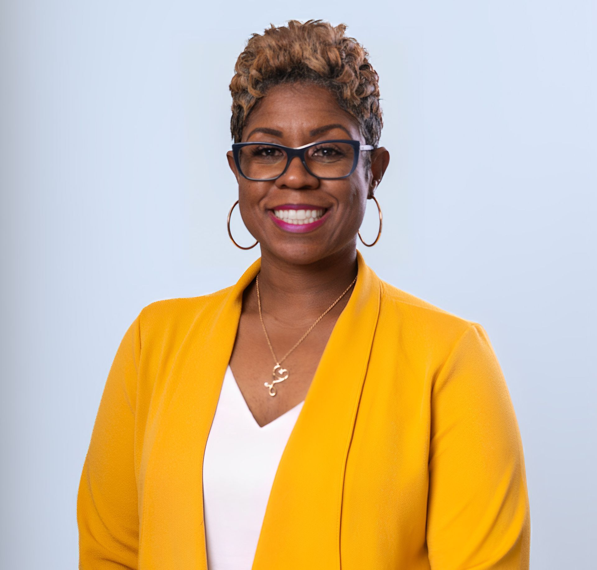 Portrait of a smiling person in a yellow blazer and glasses on a light blue background
