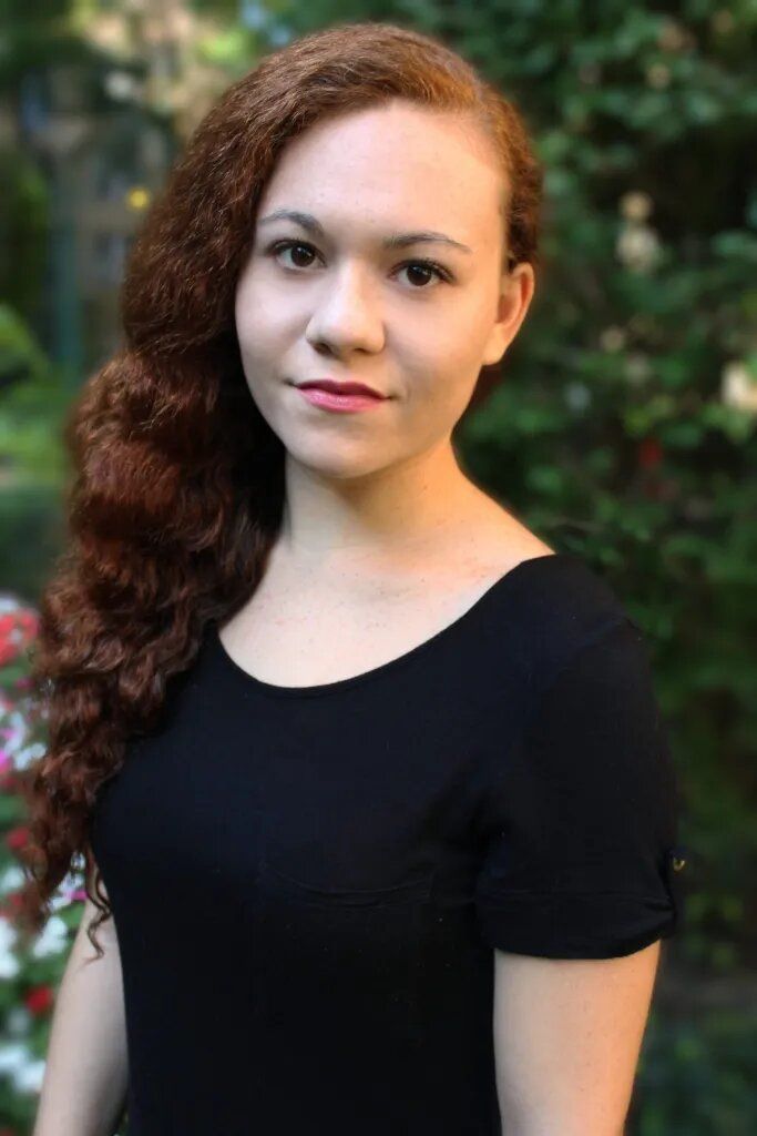 Portrait of a person in a black top, standing outdoors against a blurred green background.