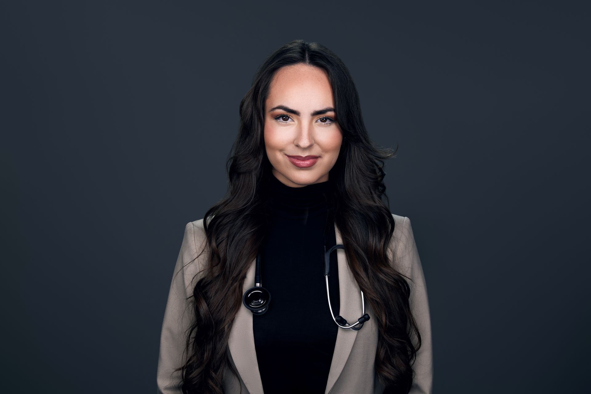Portrait of a smiling doctor in a beige blazer with a stethoscope against a dark background