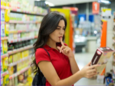 Woman in red shirt reading a product label in a supermarket aisle