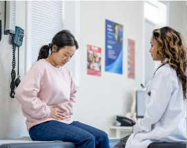 Patient clutching abdomen while talking with a doctor in a clinic room