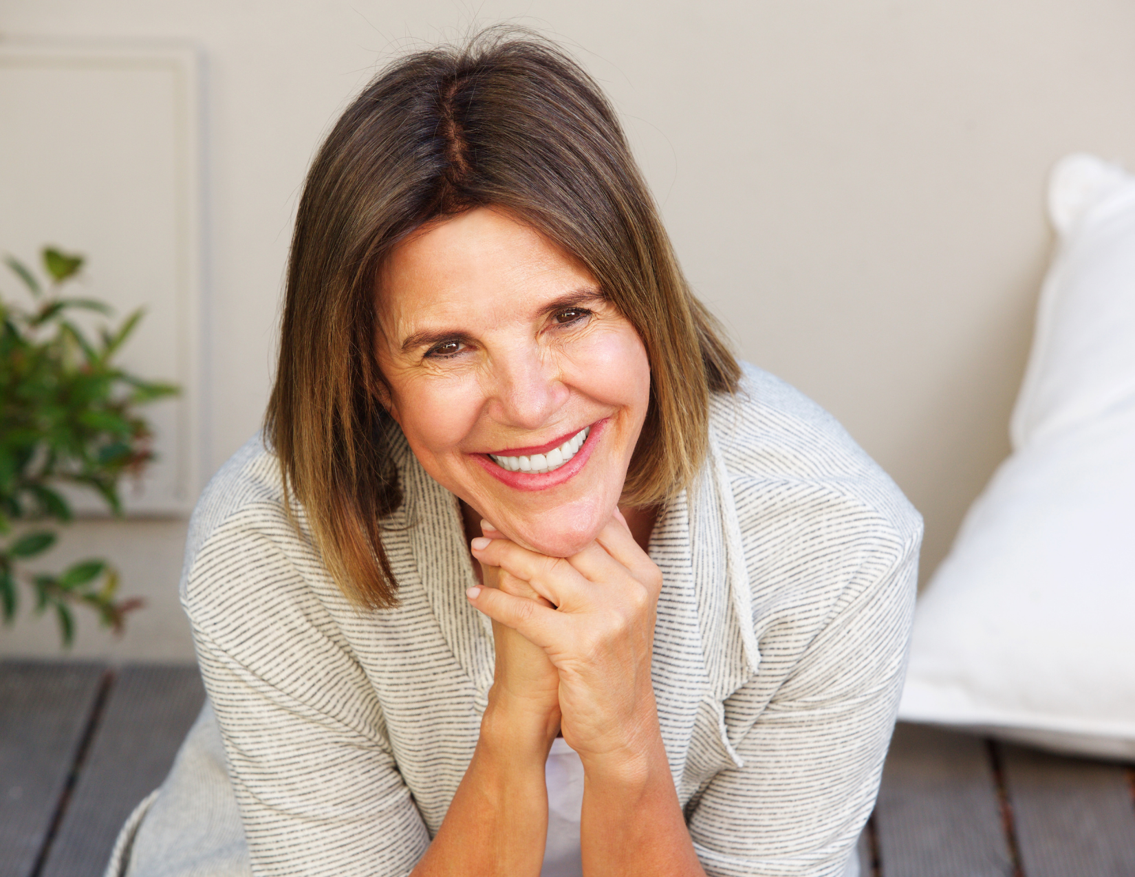 Smiling woman leaning forward with hands under chin on a couch in a bright room