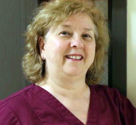 Smiling person in maroon scrubs standing indoors against a neutral background