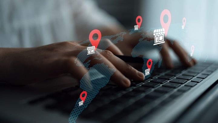 Hands typing on a laptop with digital map pins and network icons overlayed.