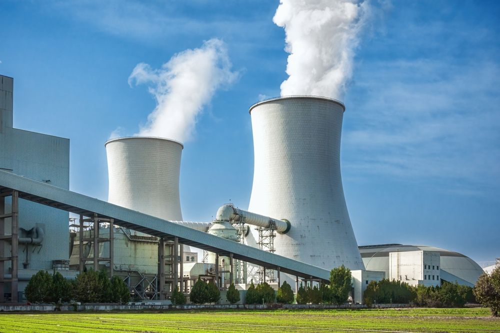 Industrial power plant with two cooling towers releasing steam under a blue sky