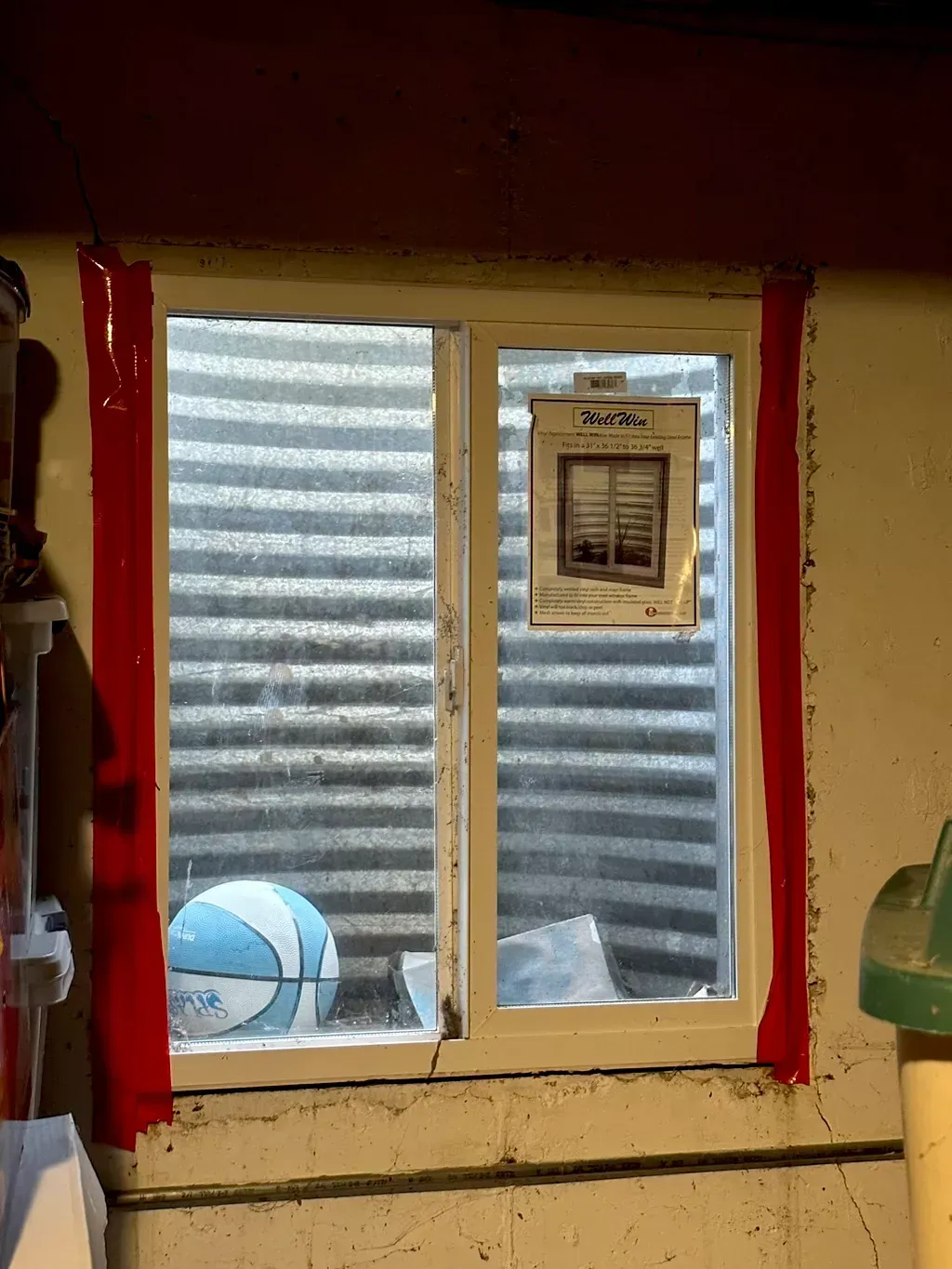 Small window with red trim and corrugated metal outside; a small framed picture hangs in the right pane.