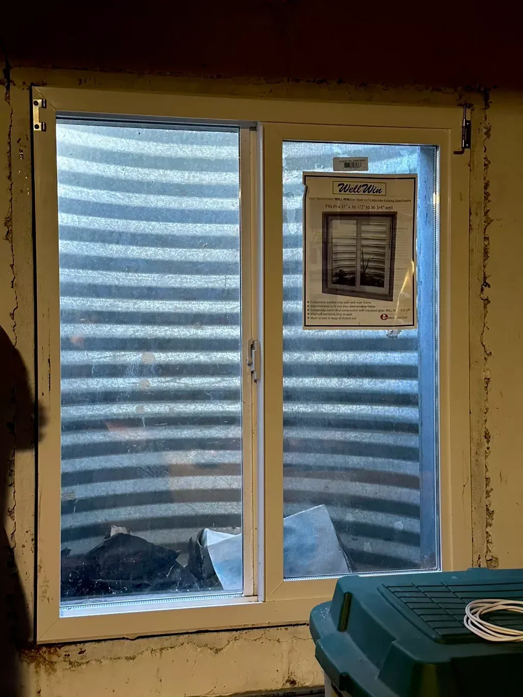 Window with blue striped exterior covering, a posted notice, and a teal bin in the foreground.