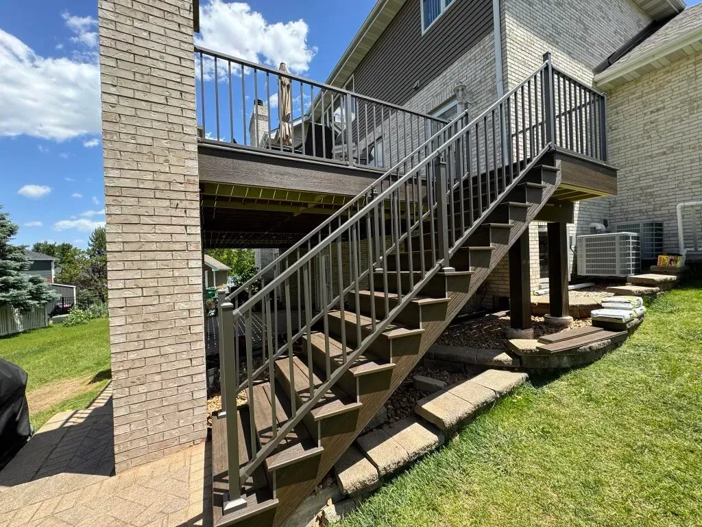 Exterior staircase with black railings beside a brick house and grassy yard