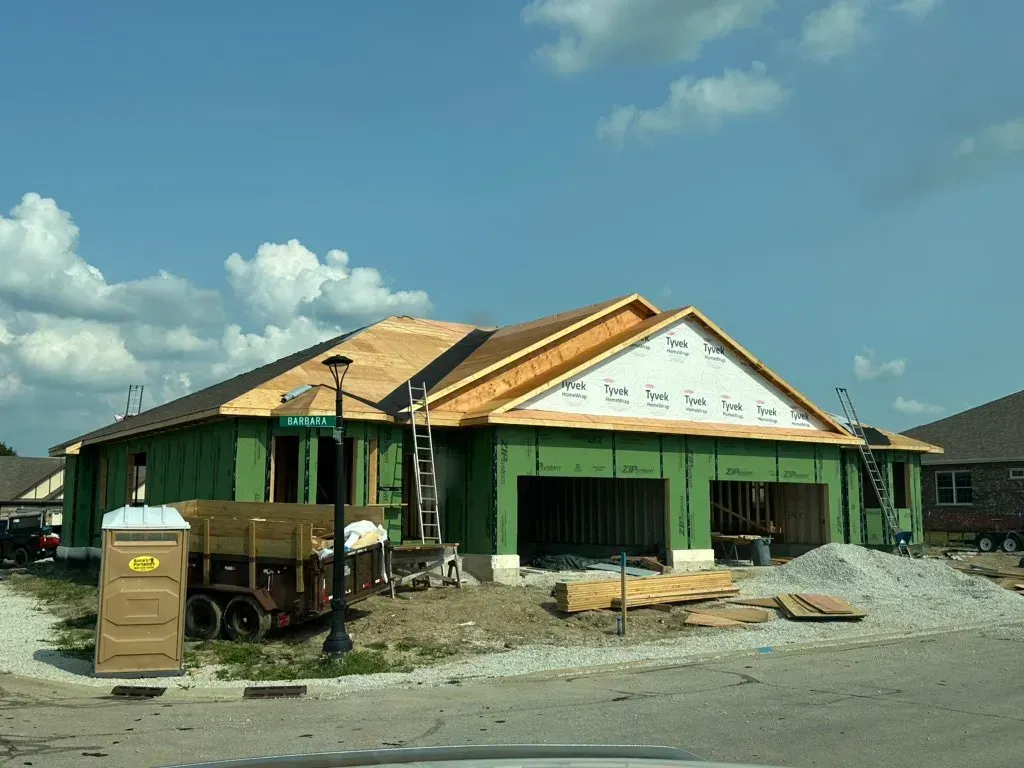 Partially built house with green exterior walls and exposed roof framing under a blue sky