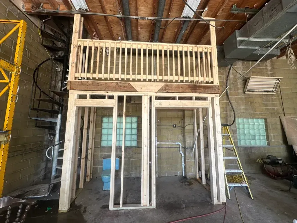 Interior of a partially built loft with a balcony, open framing, and windows under construction