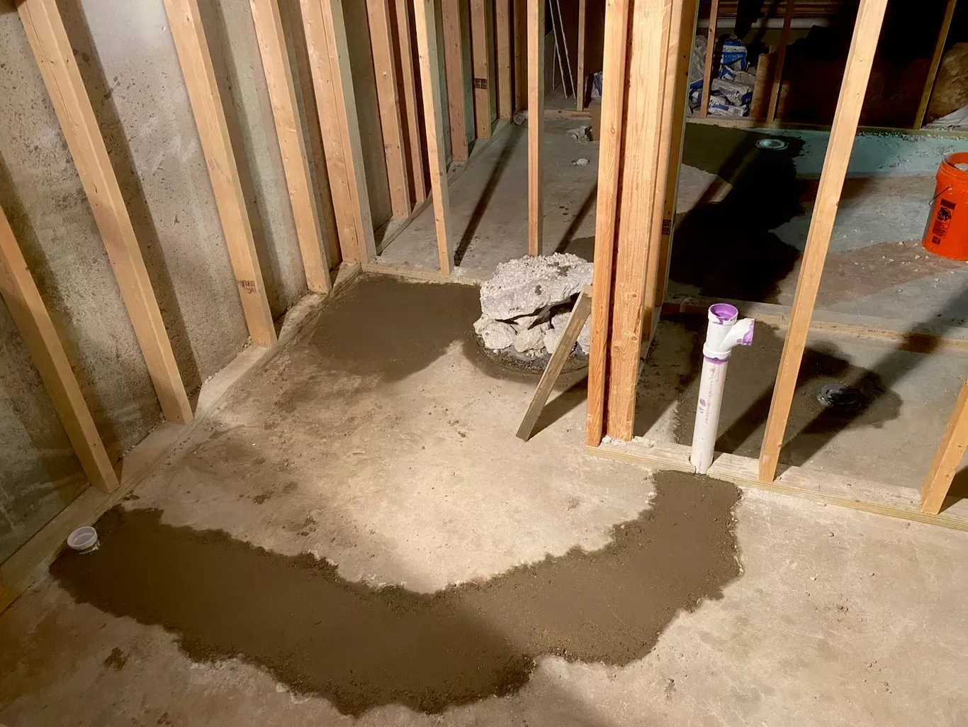Water puddle on a concrete floor inside an unfinished room with exposed wooden framing.