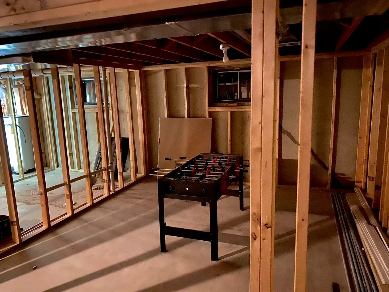 Unfinished basement with exposed wooden framing and a foosball table in the center.