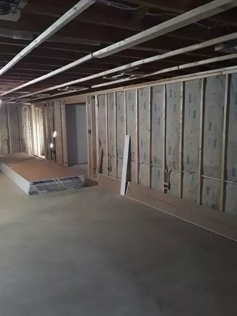 Unfinished basement with exposed ceiling beams, framed wall studs, and concrete floor.