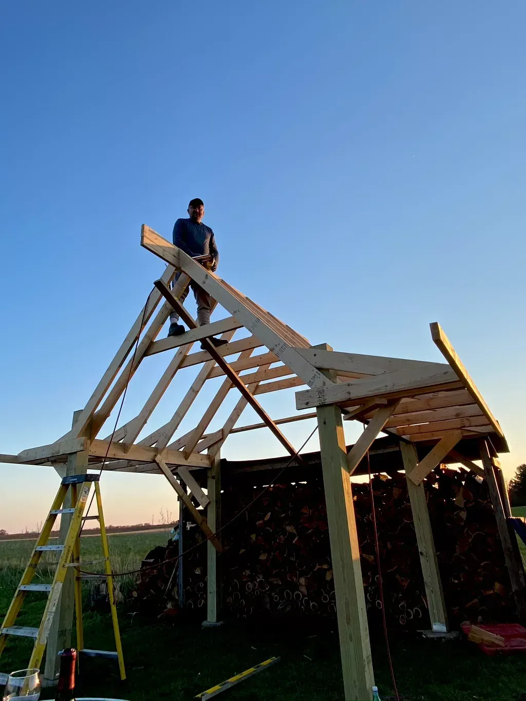 Person standing on a wooden roof frame under construction against a blue sky