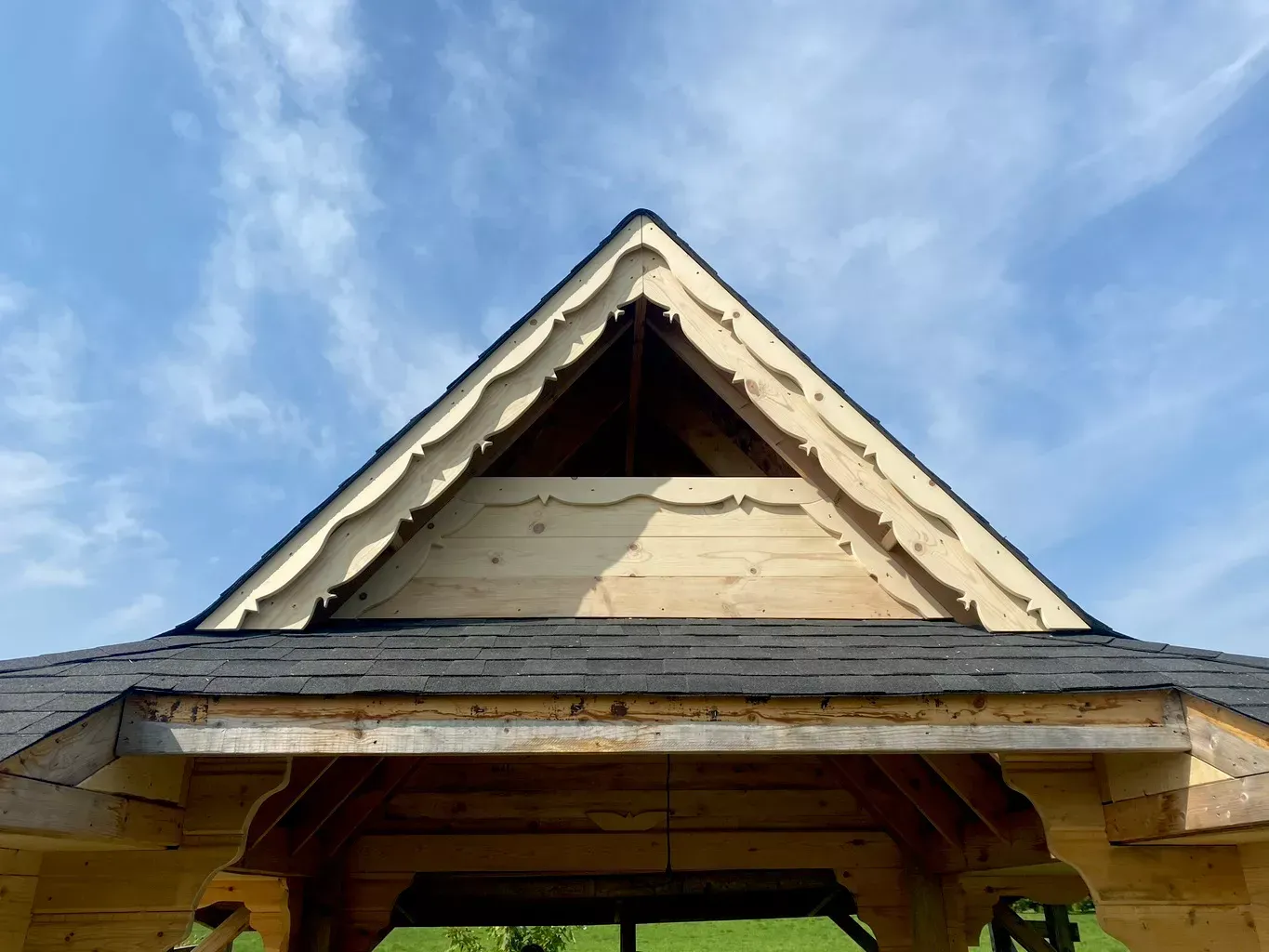Close-up of a weathered house roof peak with light siding against a blue sky