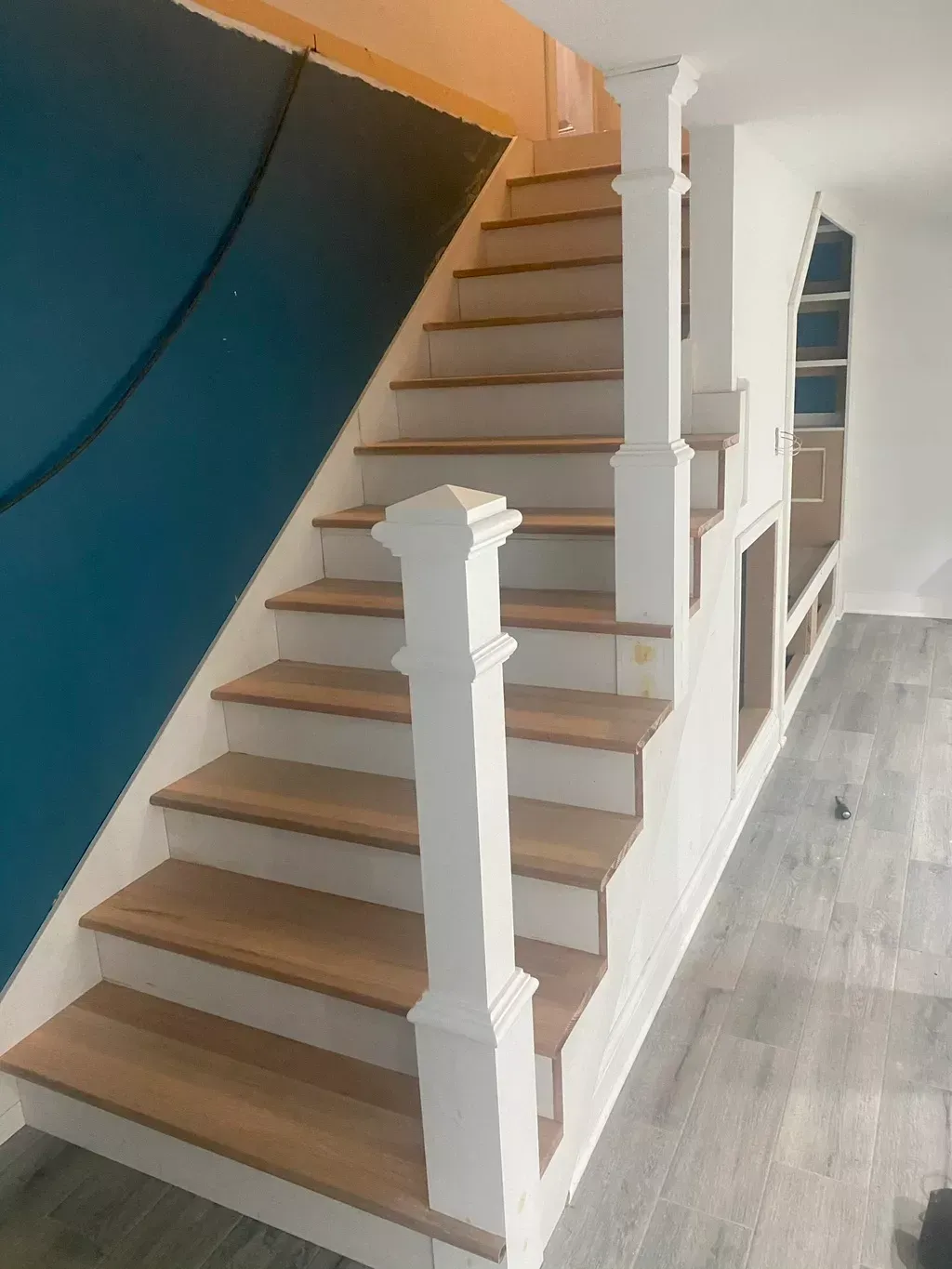 Interior staircase with white railings, wood steps, blue accent wall, and gray flooring.