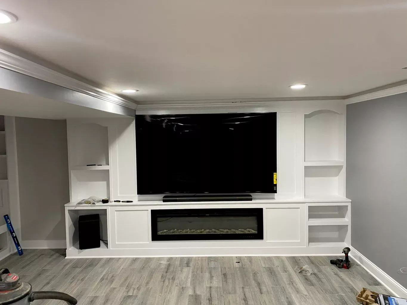 Modern living room with a built-in white entertainment center and large TV on a gray wall.
