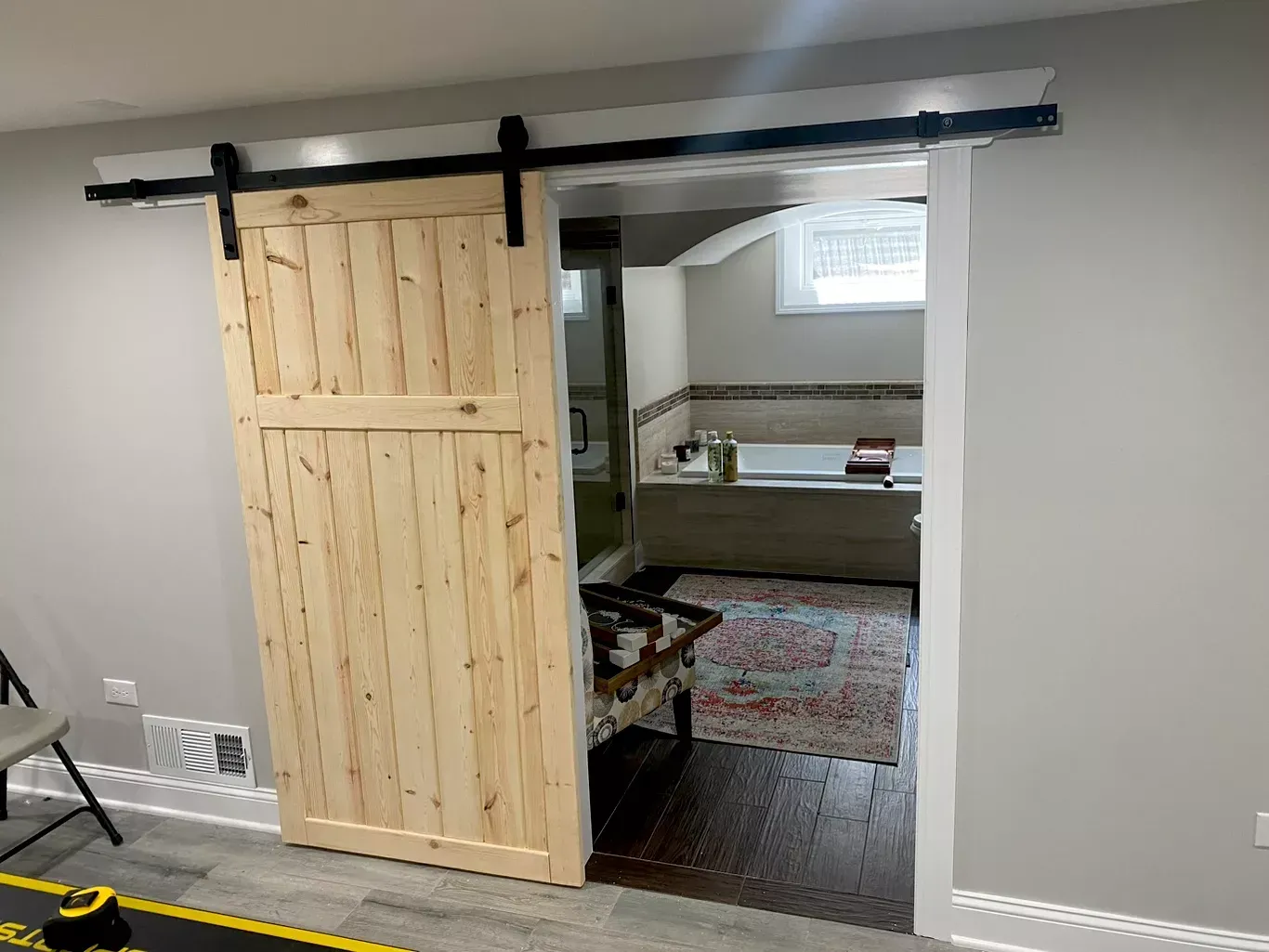 Barn door on a black track partially open to a bedroom with a bed, gray walls, and a patterned rug