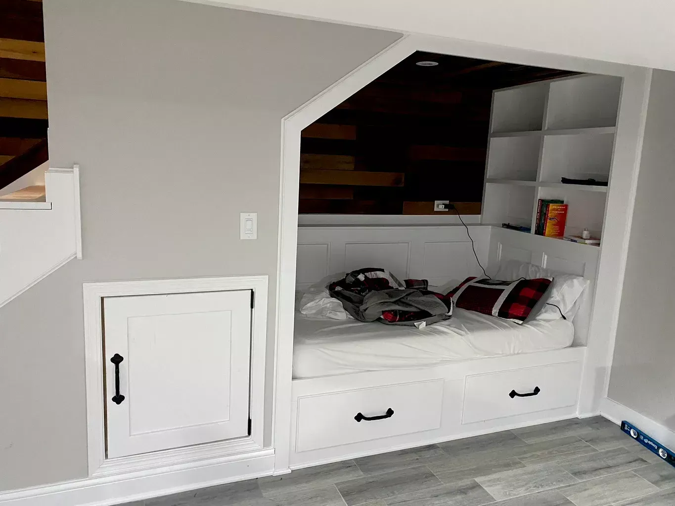 Built-in under-stair nook with a white daybed, drawers, and shelves in a small room
