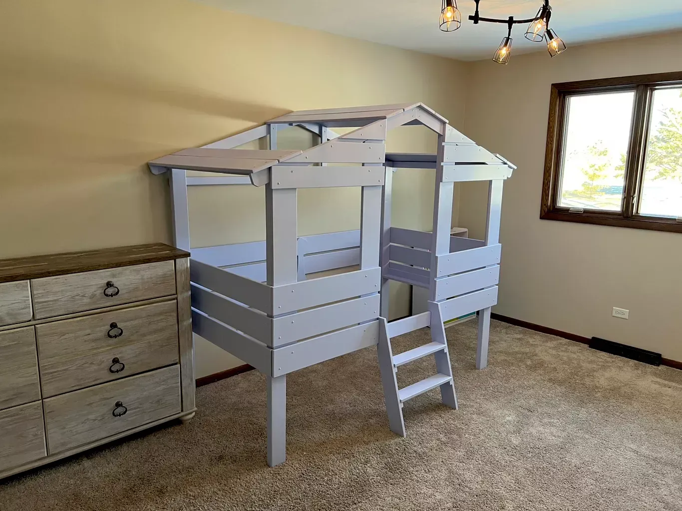 White loft bed with ladder in a carpeted bedroom next to a dresser and window