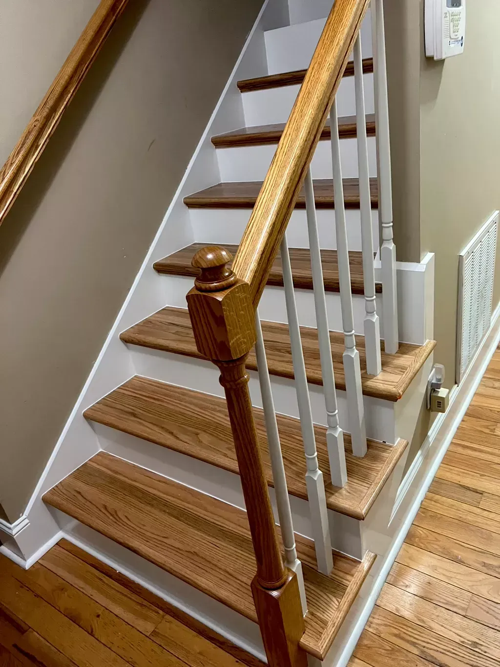 Indoor staircase with wooden steps, white balusters, and a dark wood handrail at the bottom landing