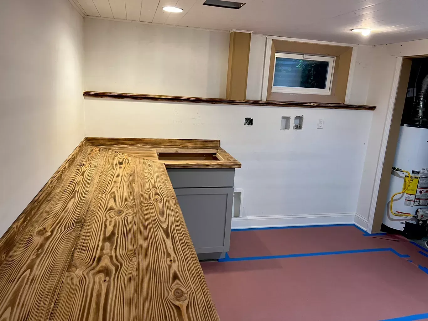 Basement under renovation with wood countertop, sink cabinet, white walls, and red floor covering