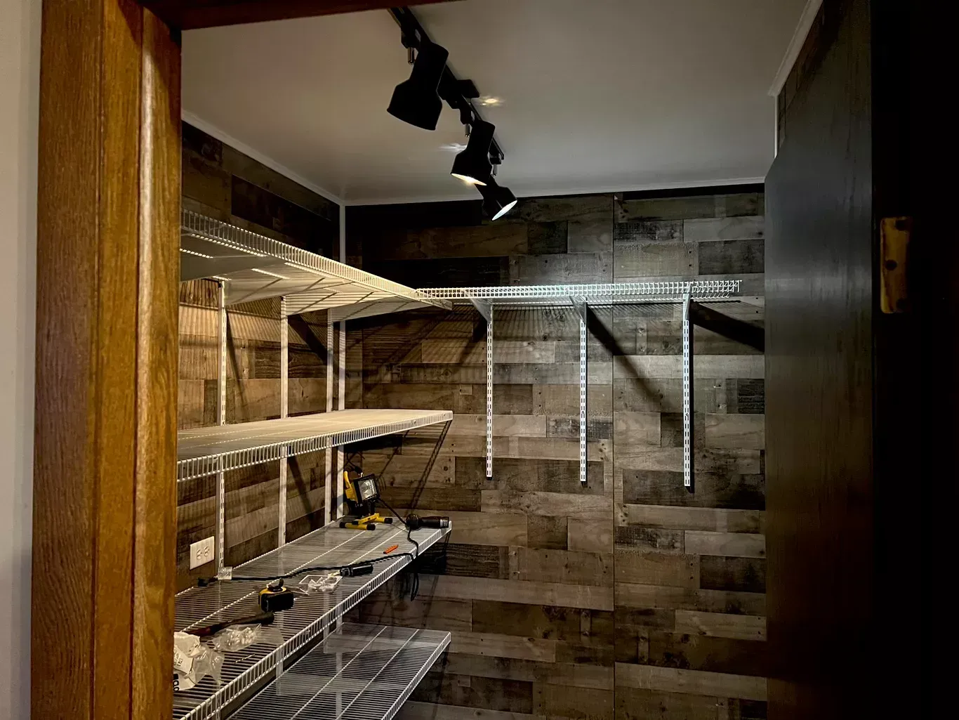 Walk-in closet with wire shelves, wood-look walls, and overhead lighting, viewed through an open door