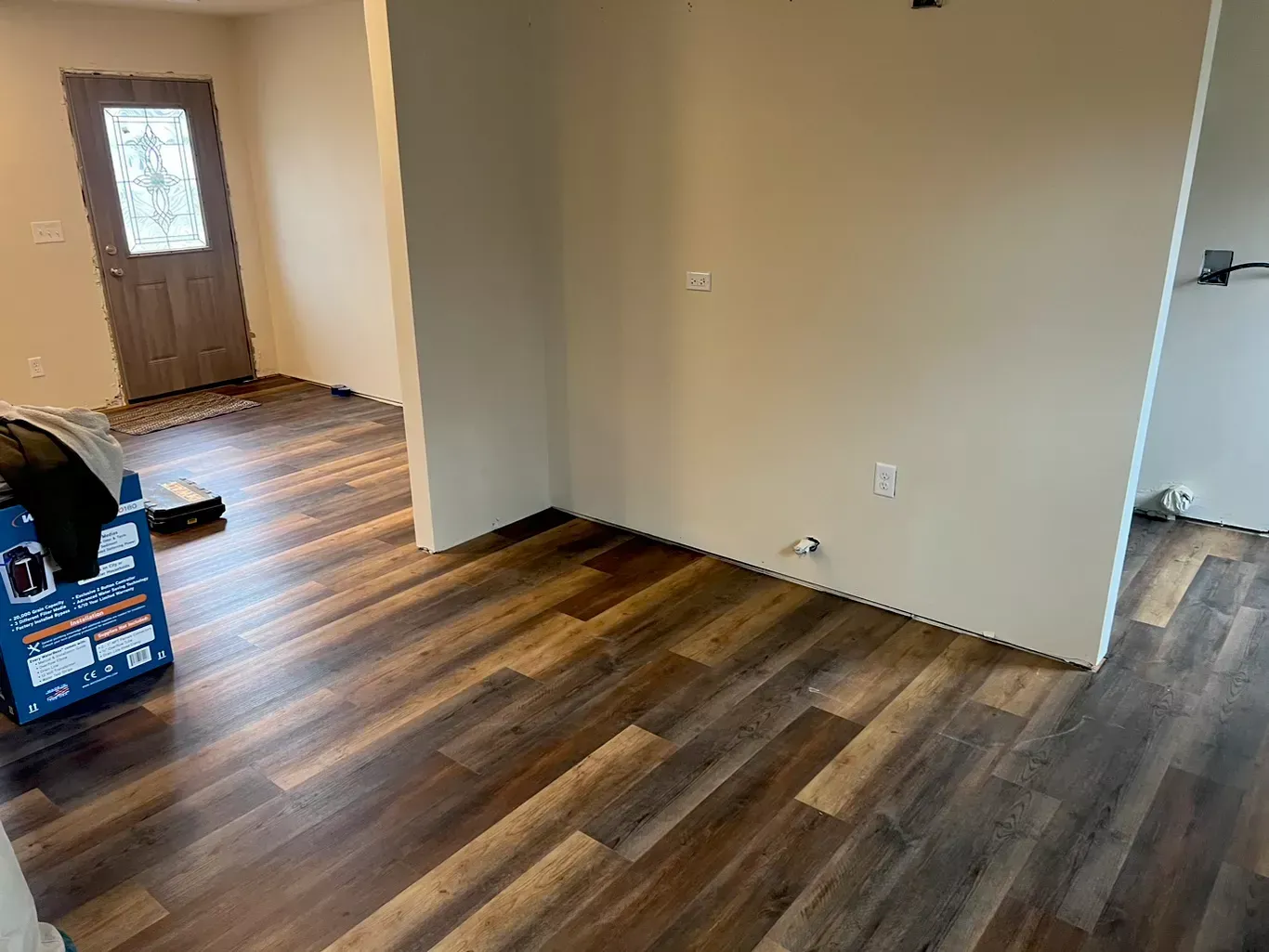 Empty living room with dark wood floors, beige walls, and an open doorway near a front door.