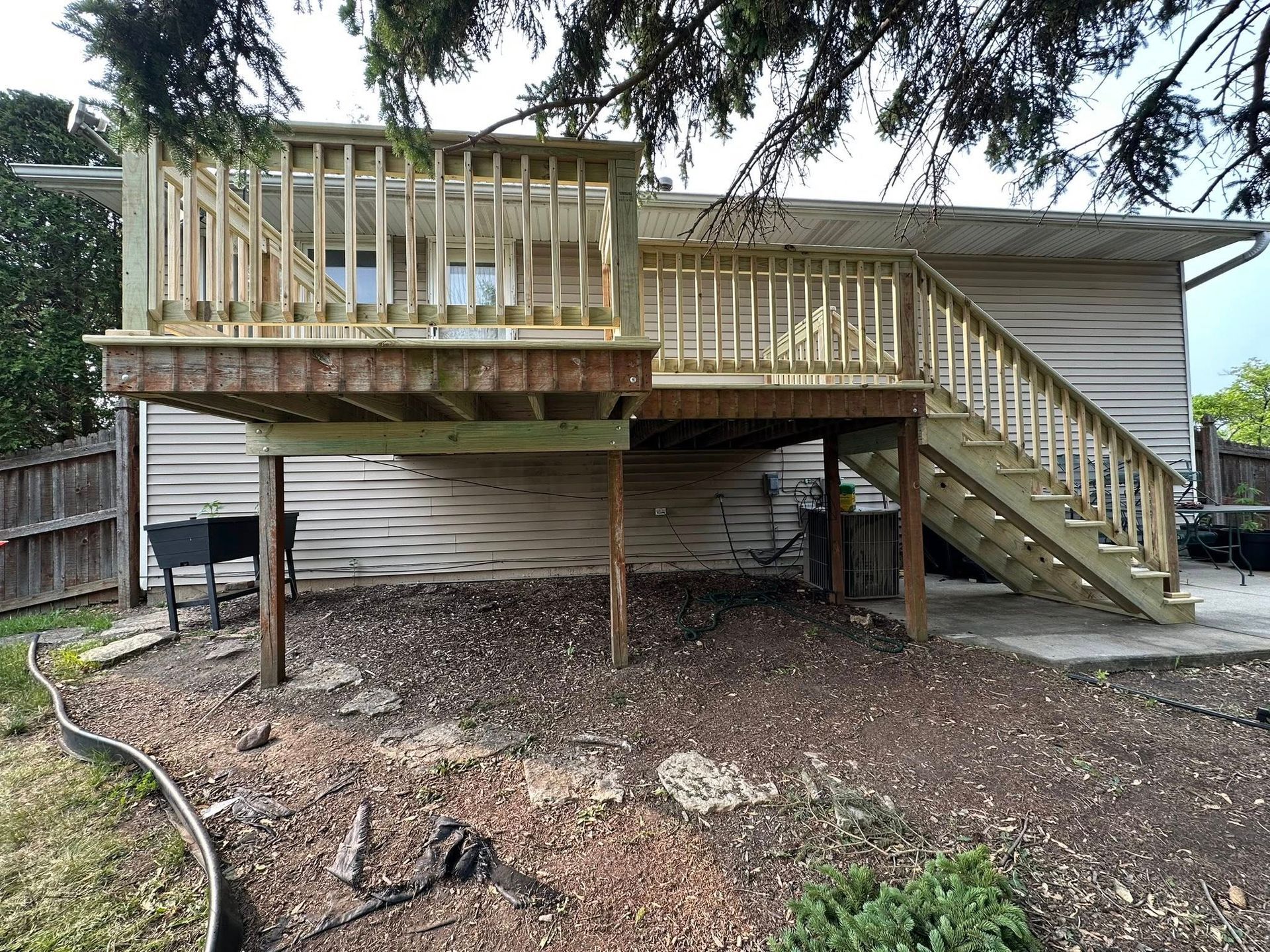 Raised wooden deck with stairs and railing attached to a house in a backyard