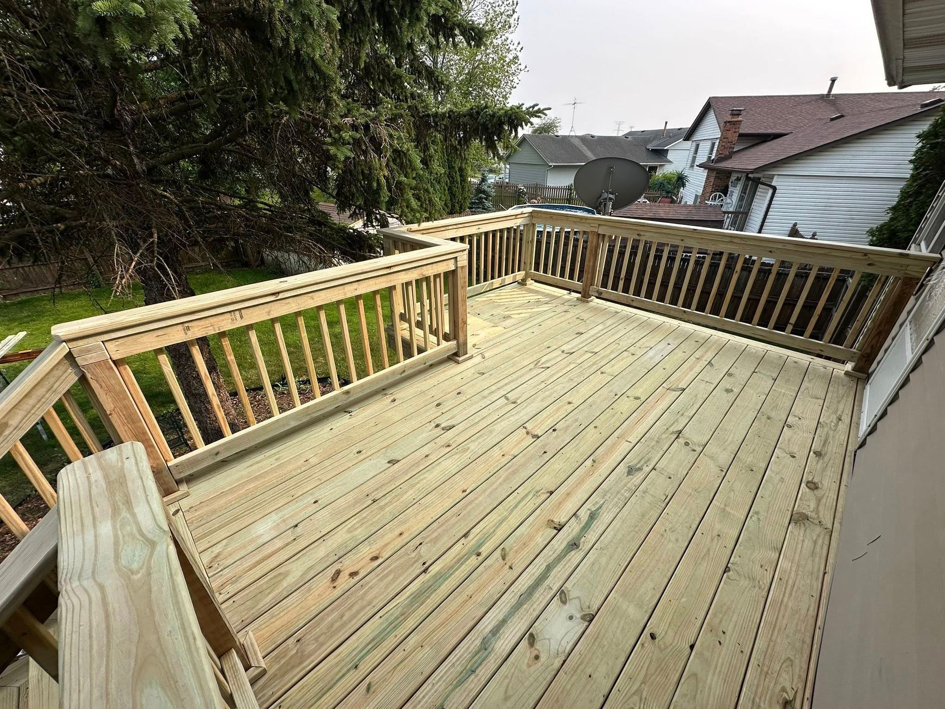 Wooden backyard deck with railings, overlooking neighboring houses and trees