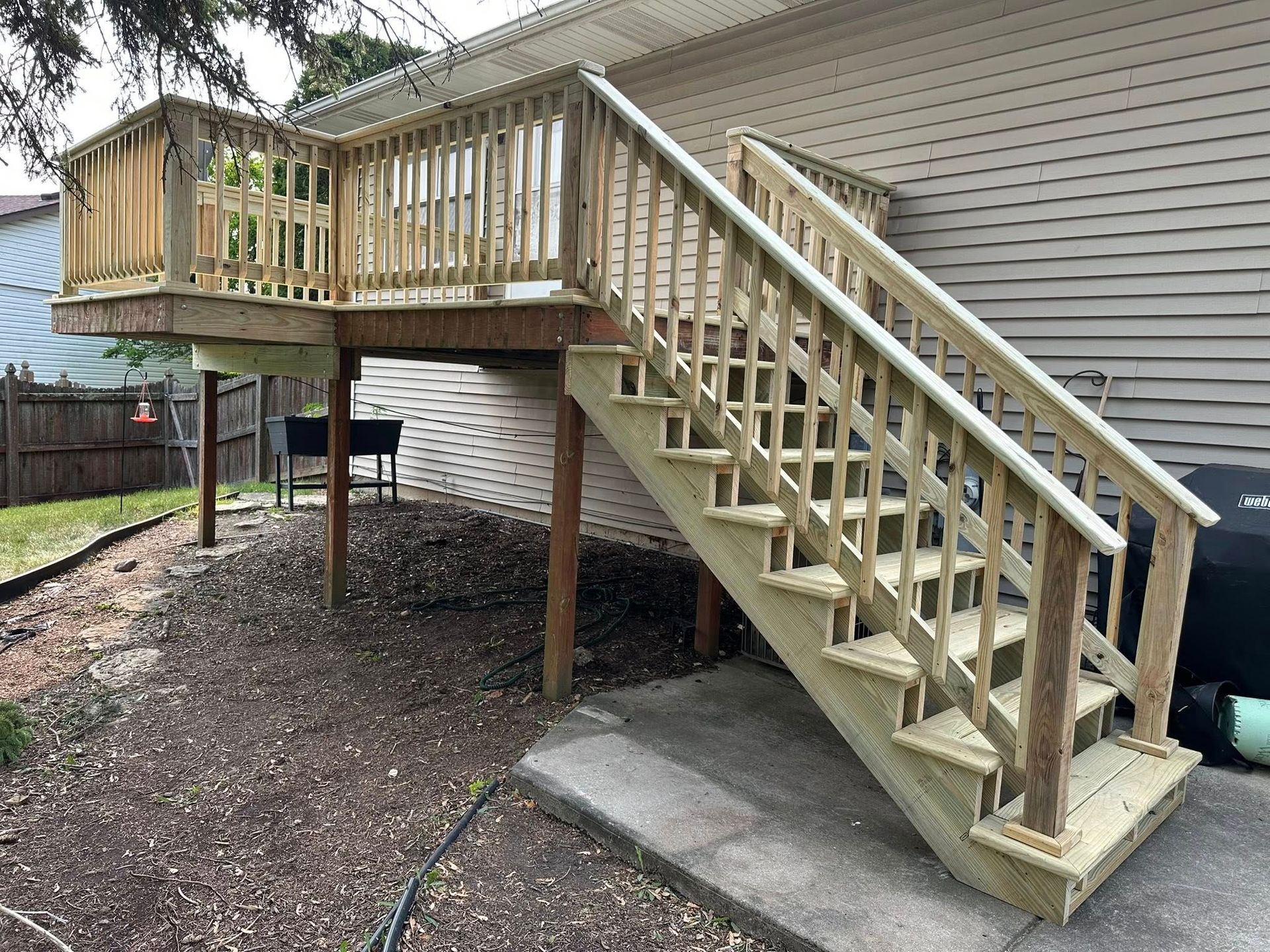 Wooden backyard deck with stairs leading down to a concrete patio beside a house