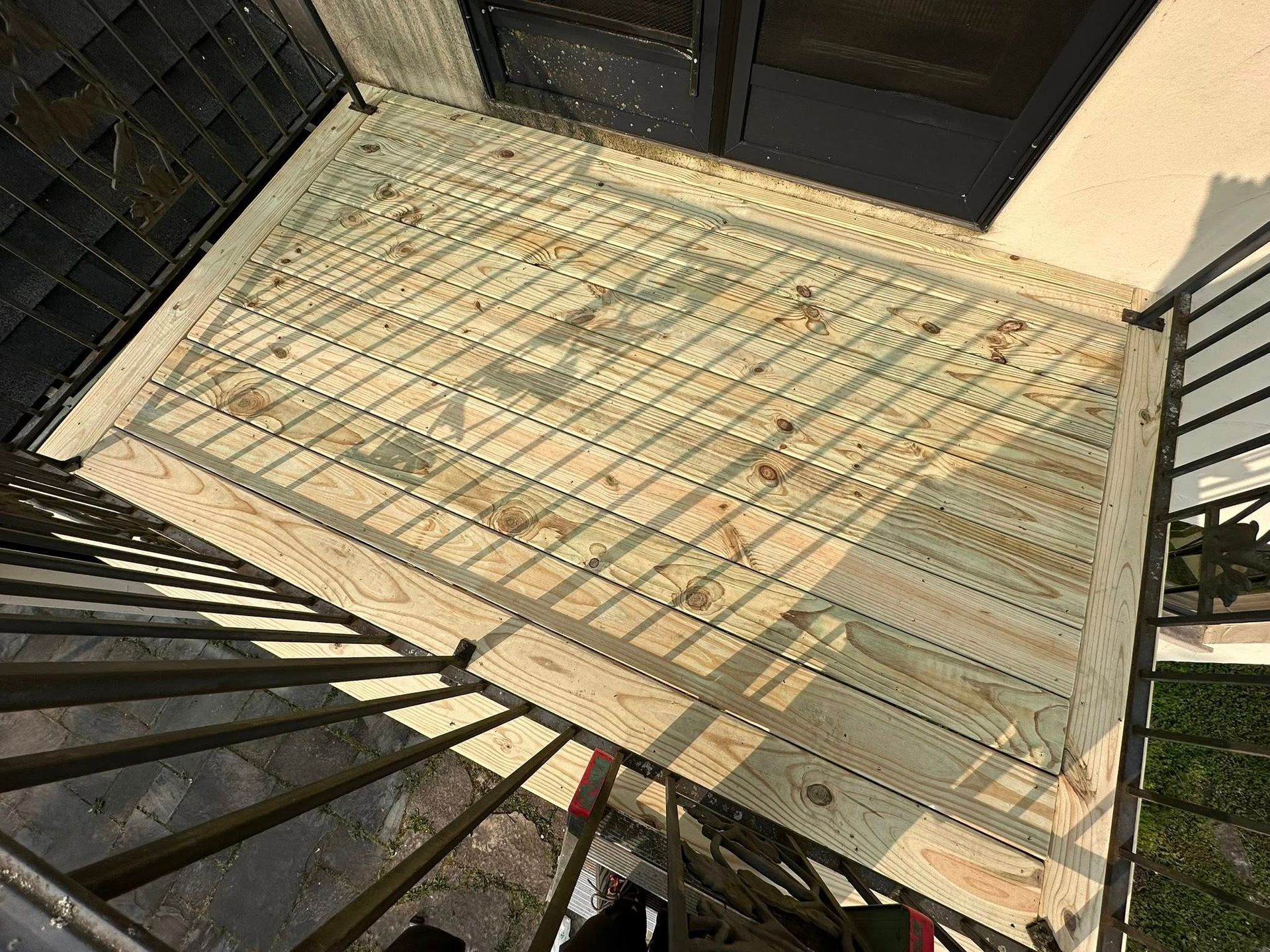 Sunlit tiled patio with black railings and a doorway at the top