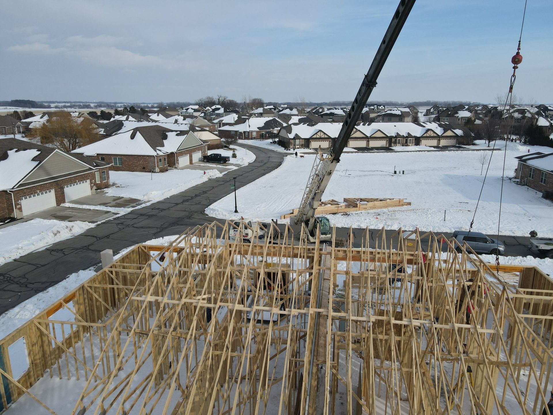 Construction site overlooking snowy suburban neighborhood with house framing in foreground
