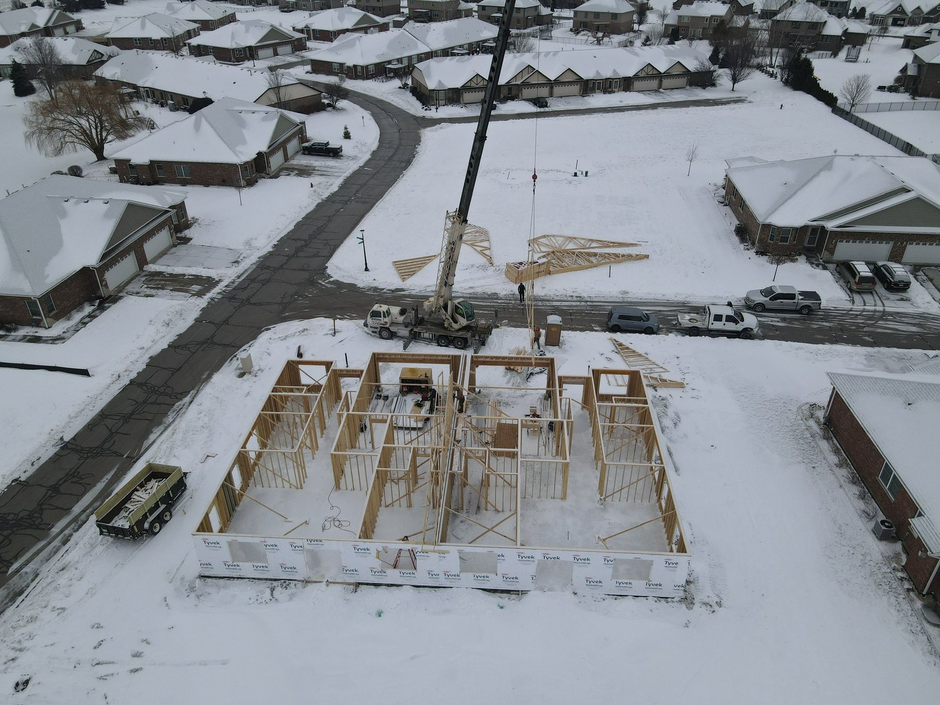 Snow-covered construction site with a partially built wooden structure in a residential neighborhood