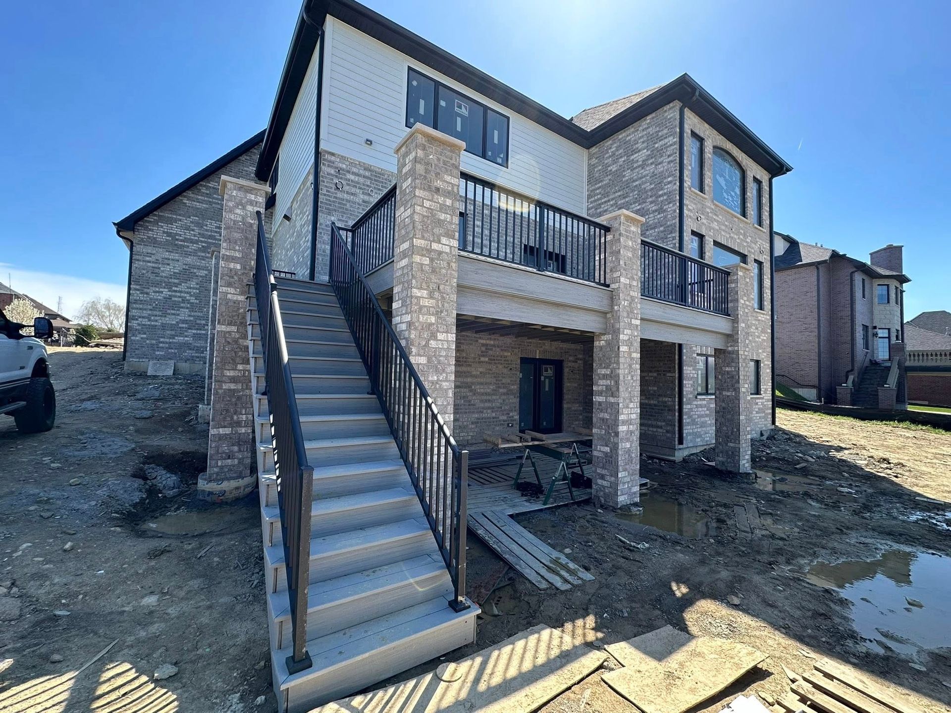 Two-story stone house under construction with exterior stairs and unfinished landscaping