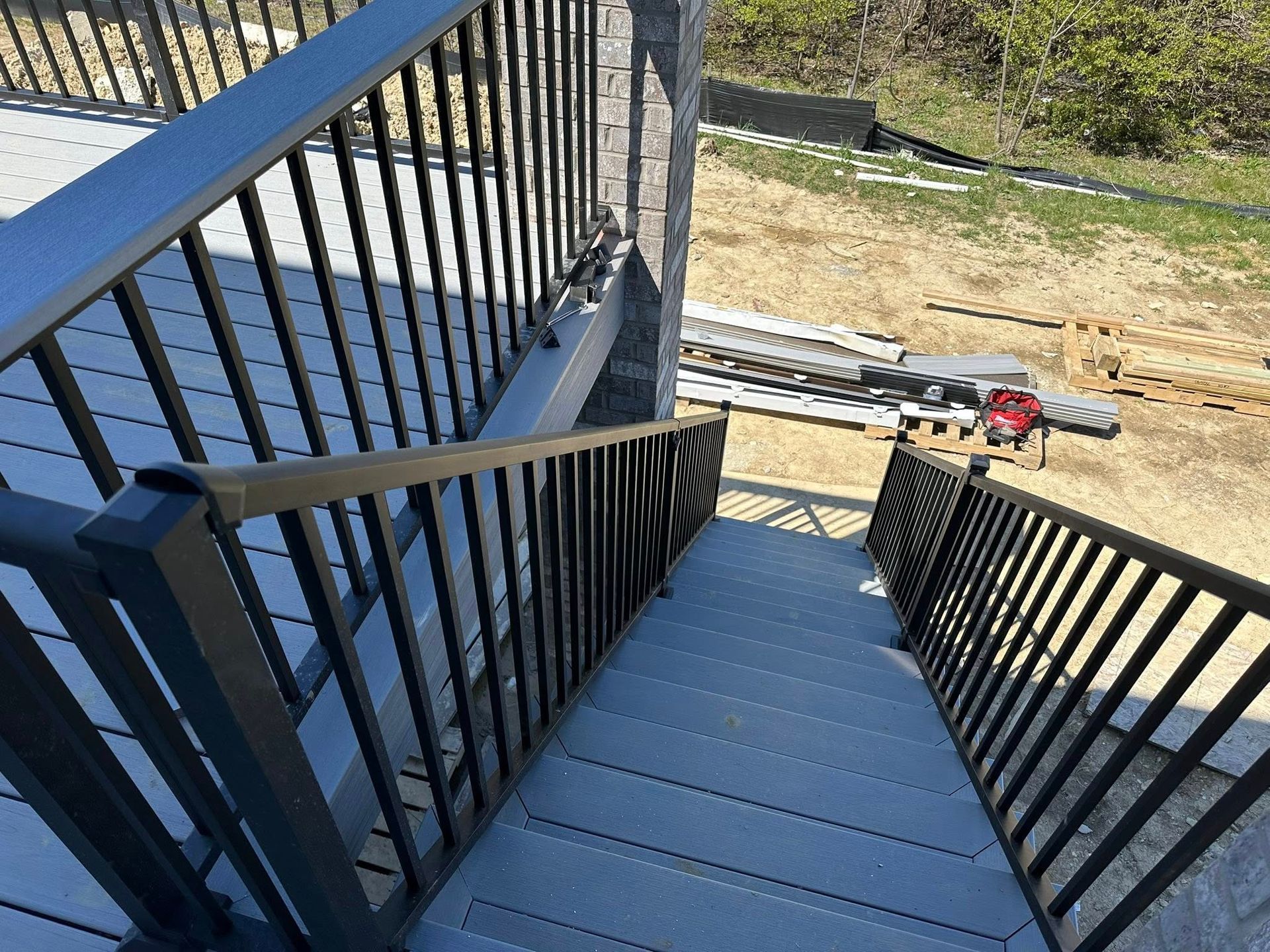 Blue staircase with black railings leading down to a yard with construction materials.