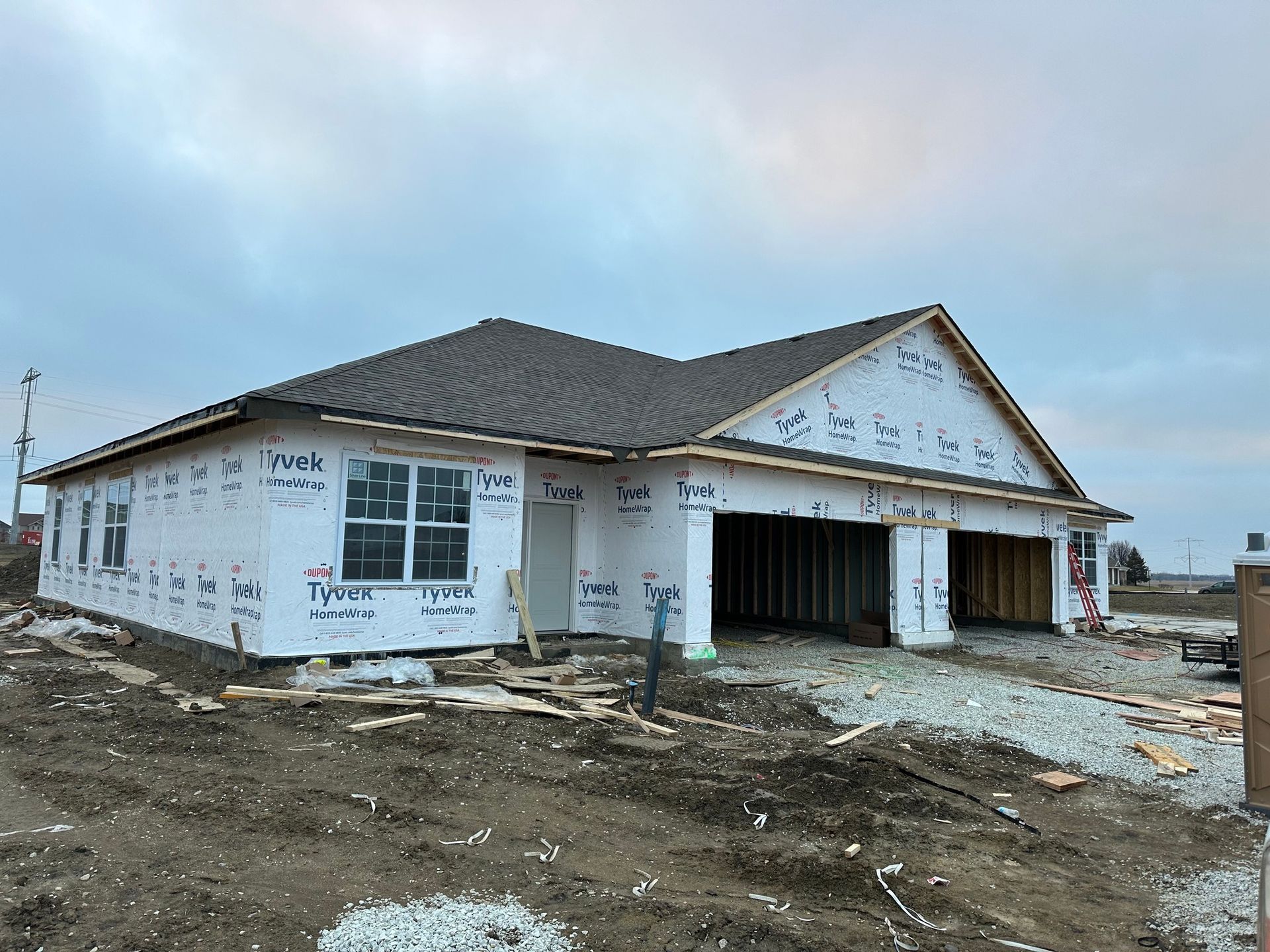 Unfinished single-story house under construction with exposed sheathing and bare dirt around it.
