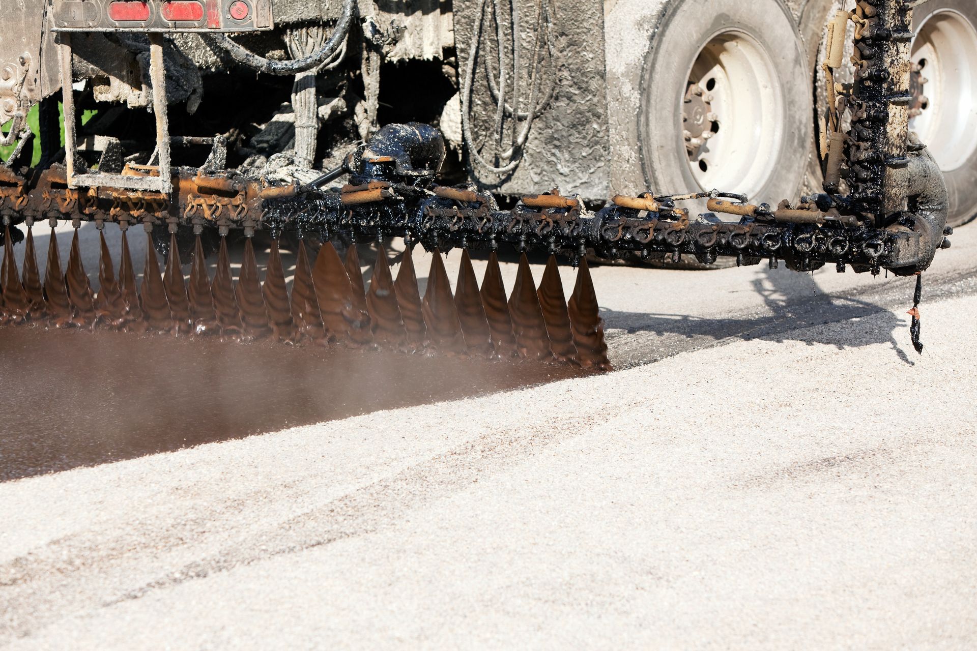 Asphalt distributor spraying emulsion on a gravel road.