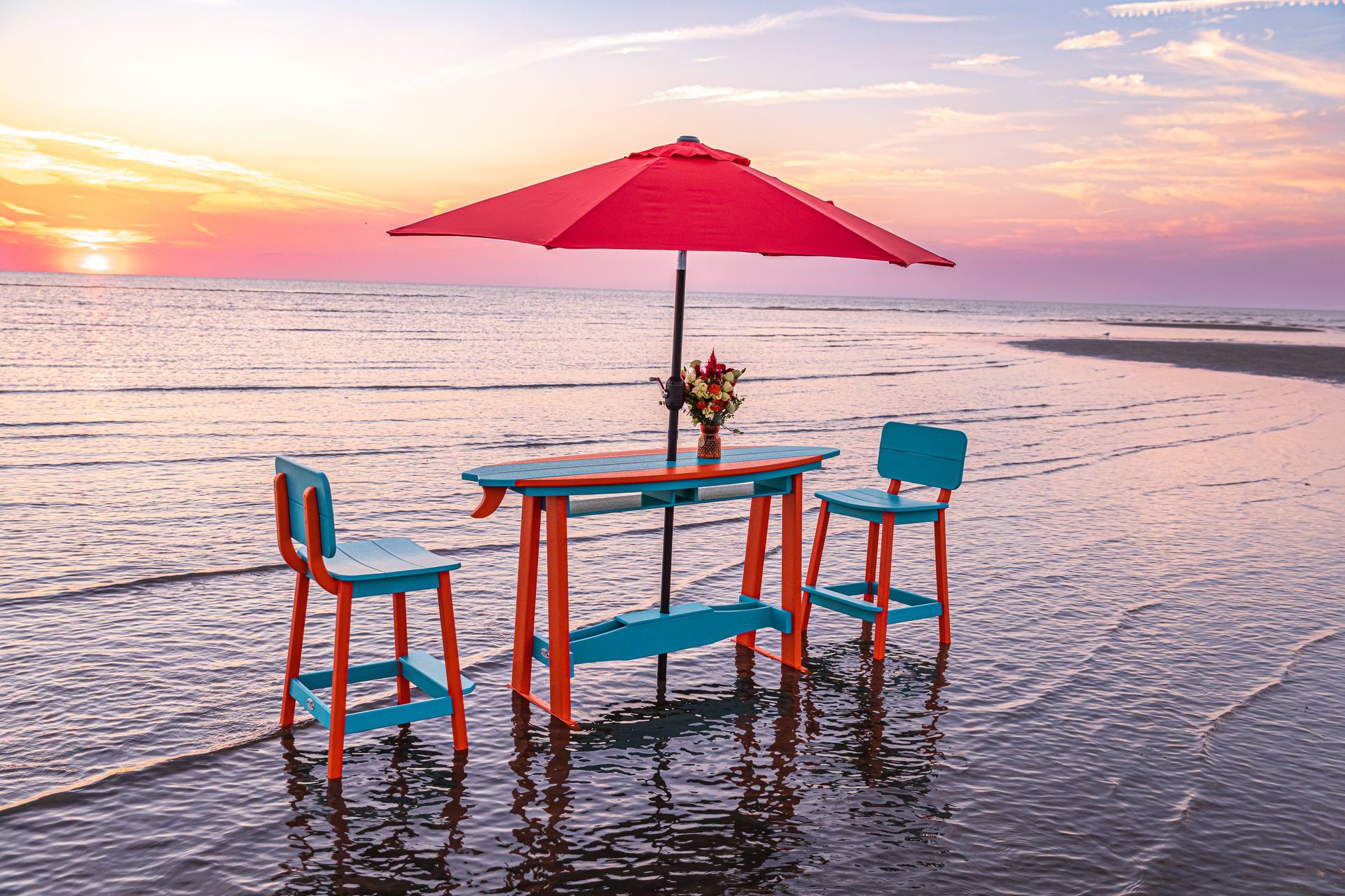A table and chairs under an umbrella on a deck overlooking the ocean.