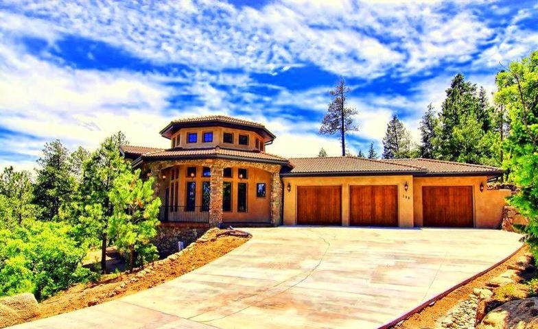 A large house with a driveway leading to it is surrounded by trees and a blue sky.