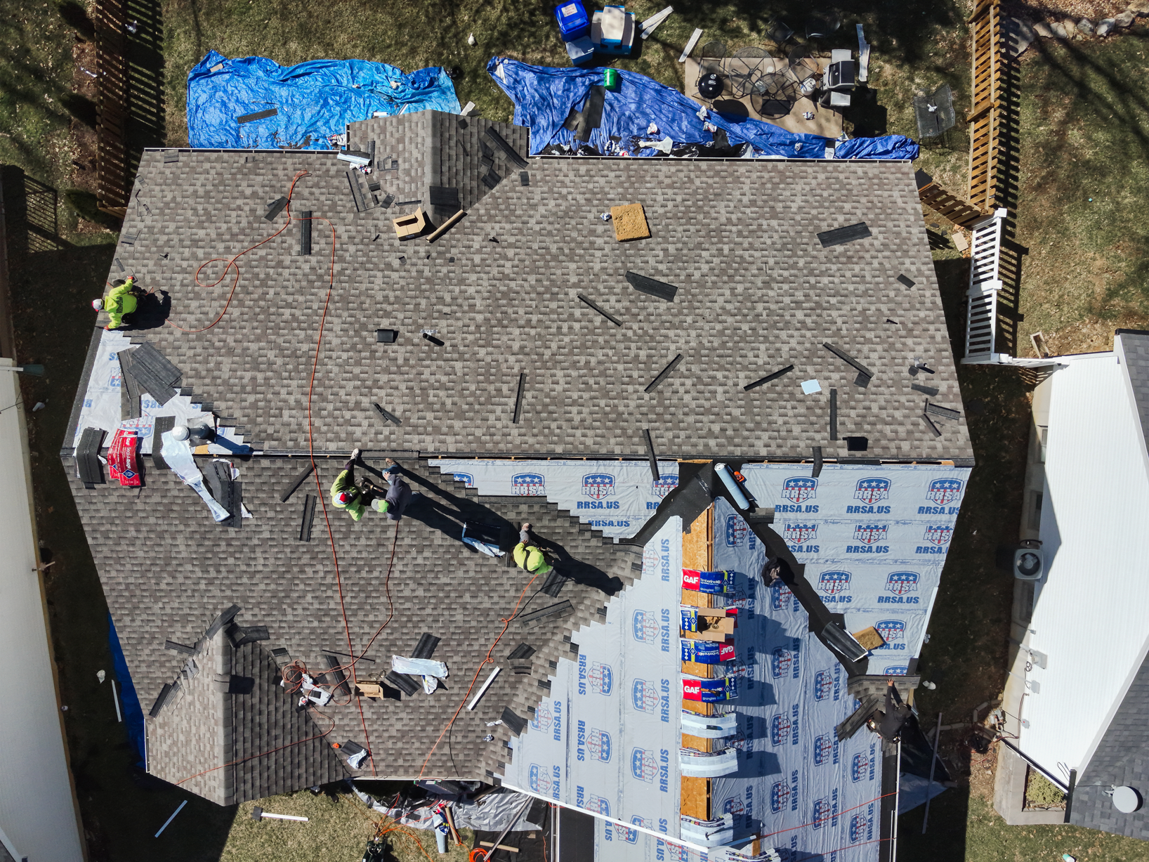Aerial view of a house roof under construction; roofers in safety vests work on the shingles.
